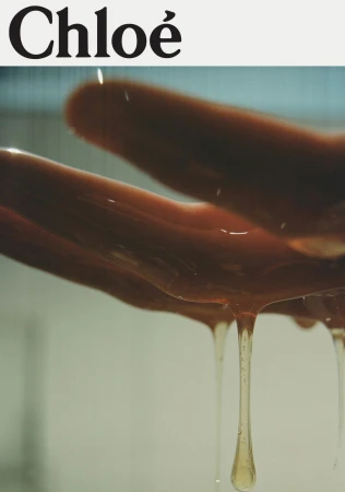 Close-up of a hand with viscous liquid dripping down, conveying a sense of richness and texture, set against a minimalist backdrop.