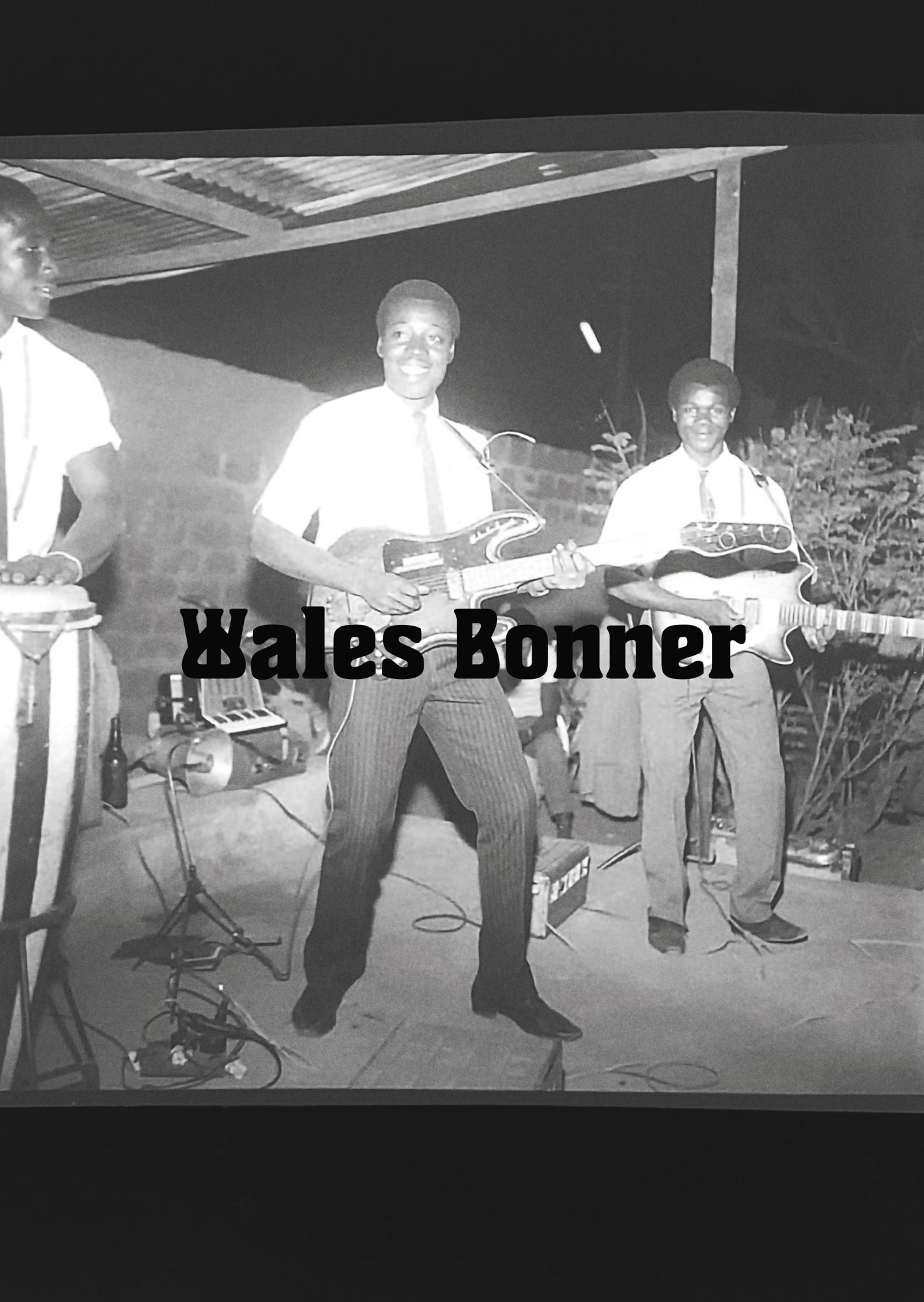 Black and white outdoor shot of three adult musicians performing: one plays drums, two play electric guitars, with Wales Bonner text overlay.