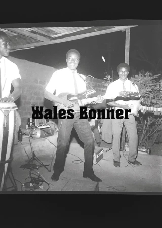 Black and white outdoor shot of three adult musicians performing: one plays drums, two play electric guitars, with Wales Bonner text overlay.