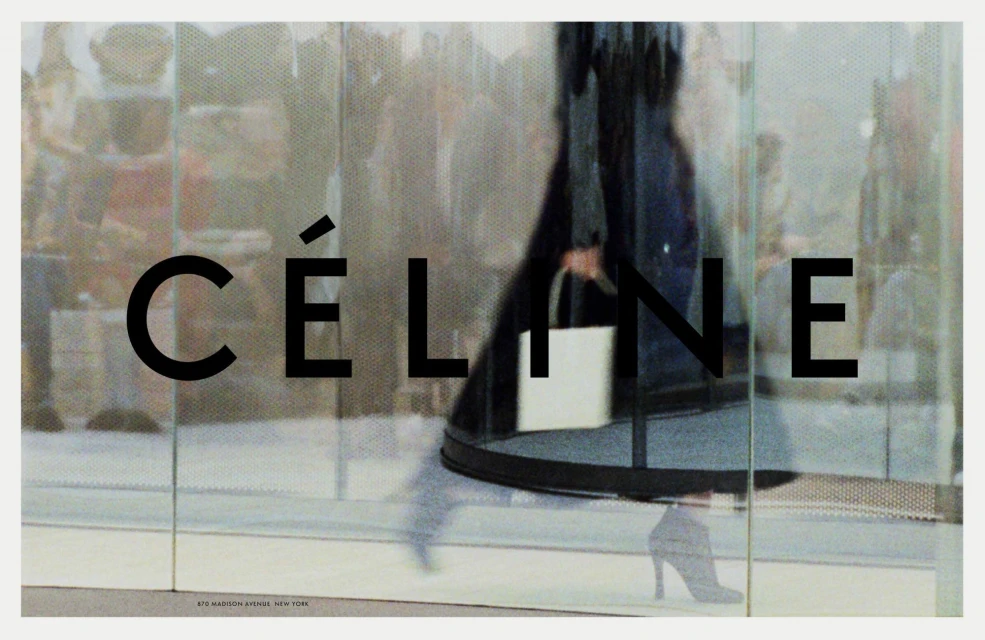 Fashion advertisement featuring a woman in heels and dark coat carrying a white handbag, walking past large Celine branded glass door.