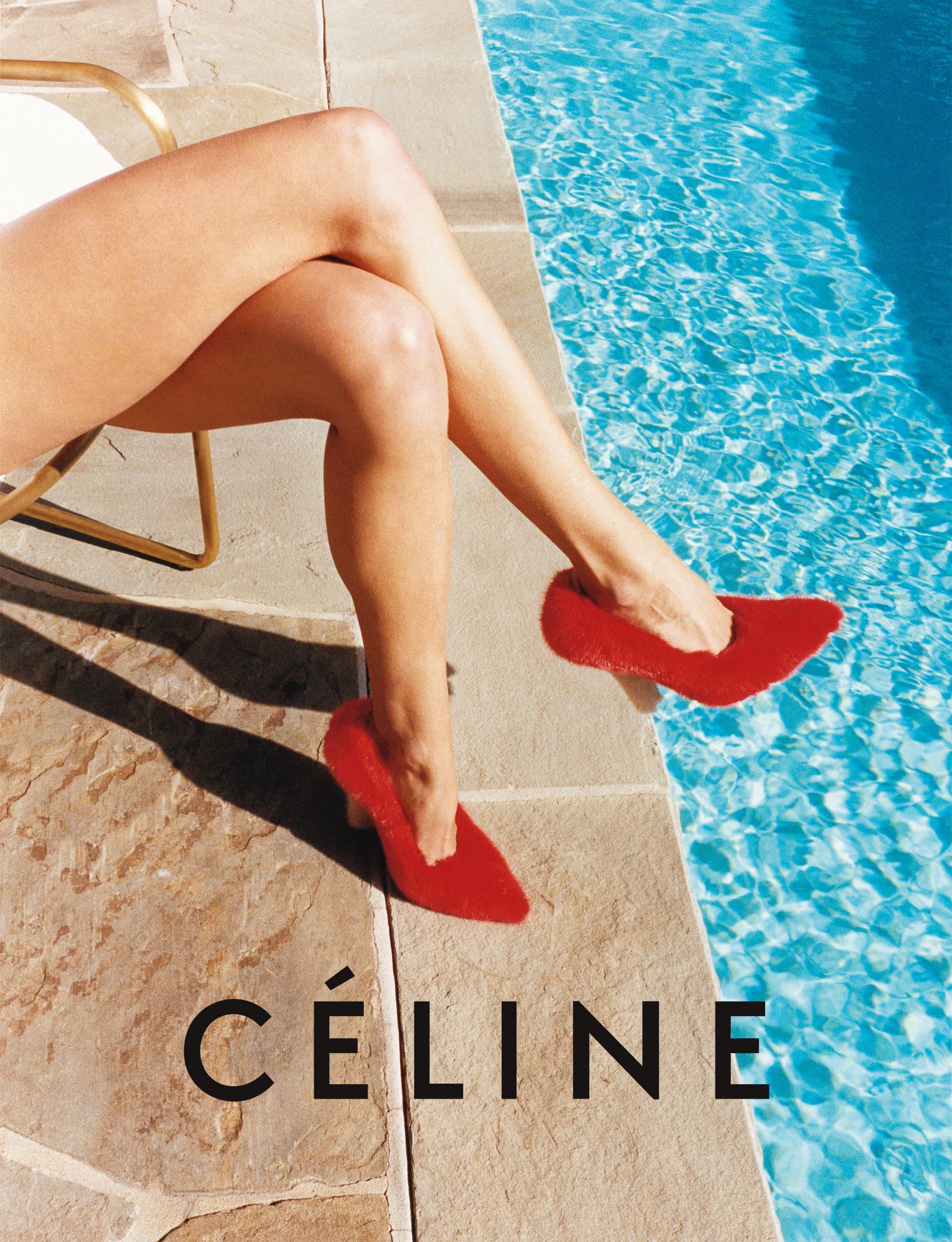 Woman's legs and red furry heels on a stone patio next to a pool, featuring a Celine logo for fashion advertising and promotion.
