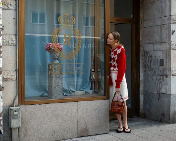Woman in red and white cardigan looking at a shop window displaying a floral bust and 'Regal Professional Hair Care' text.