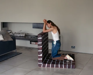Woman kneeling on a painted brick prop in a minimalist living room, photographed by Nigel Shafran