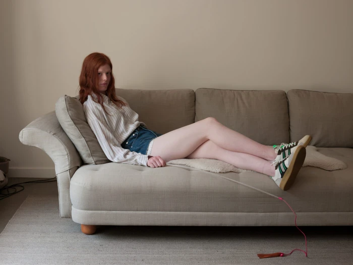 Red-haired woman reposing on a beige couch wearing striped shirt and sneakers