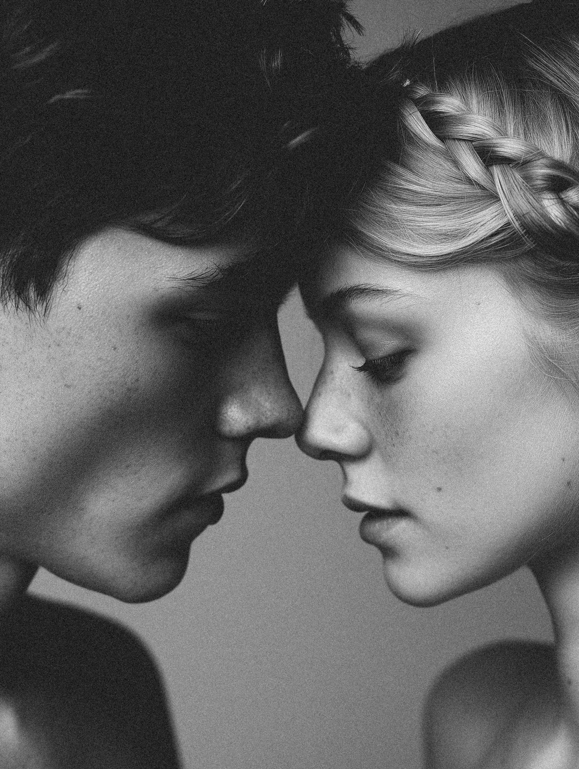 Close-up black-and-white portrait of a young adult couple with their faces close together, the woman with braided blonde hair.