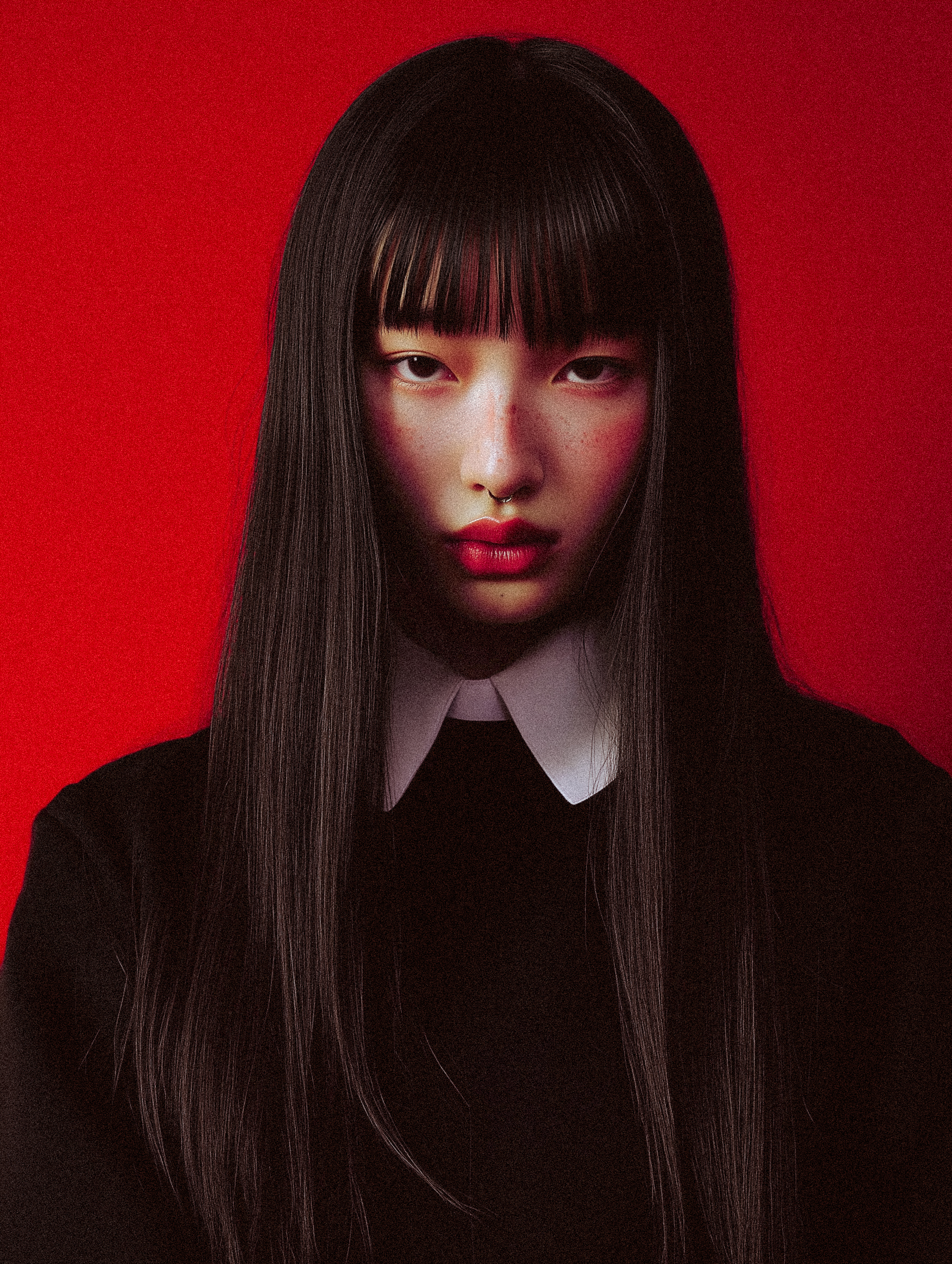 Portrait of a young Asian woman with long dark hair, red lips, wearing a black top with a white collar, set against a red backdrop.