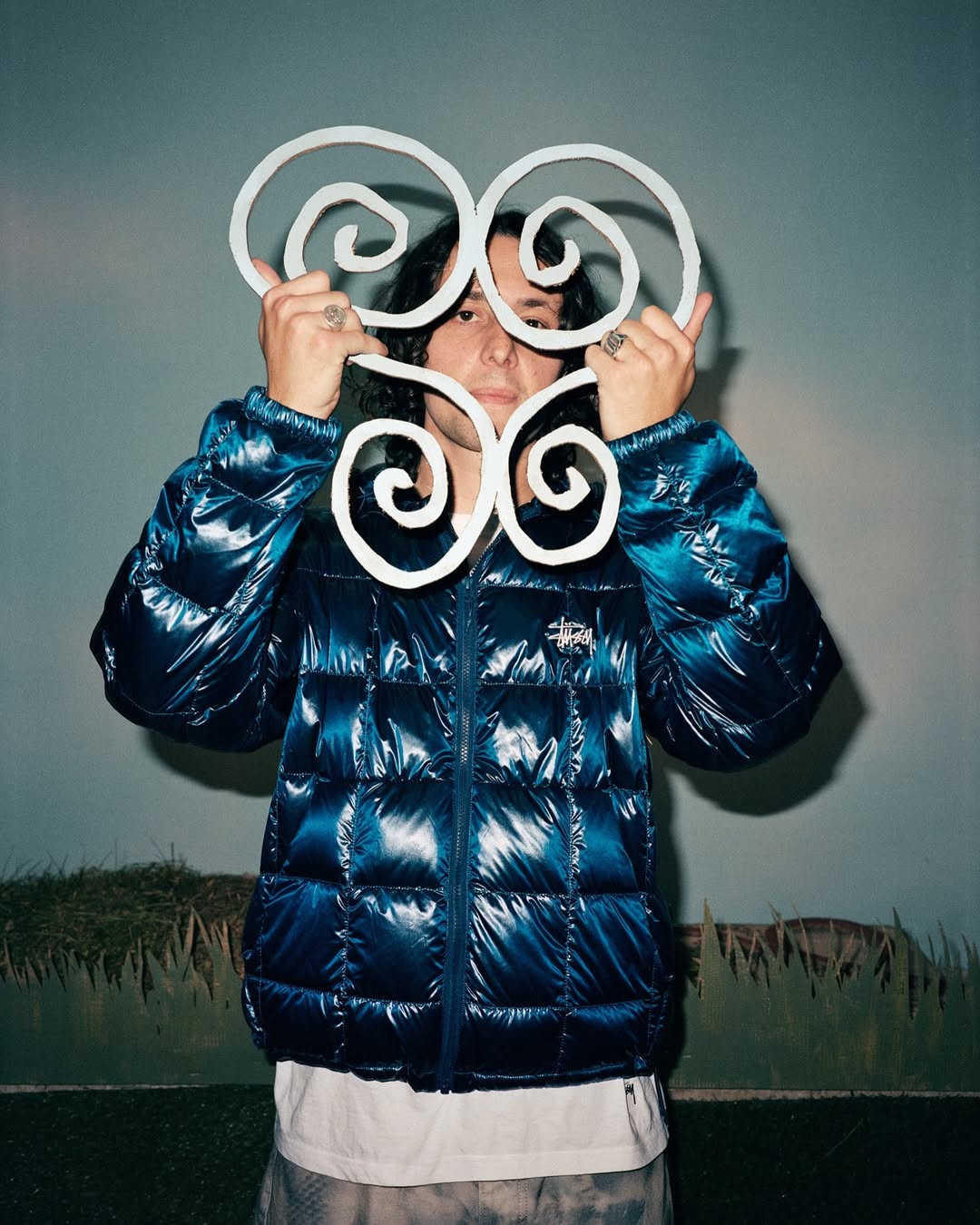 Person in puffer jacket holds up decorative, white, spiral design. Indoor portrait with soft lighting. Neutral background.