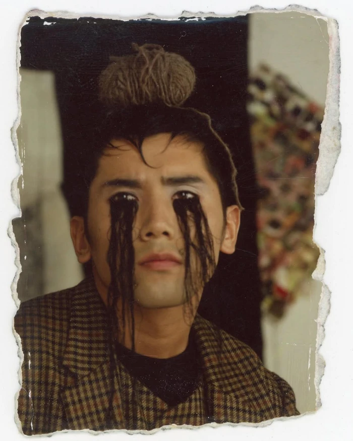 Portrait of a man wearing a plaid blazer with dark strands streaming from his eyes, photographed by Mark Lebon.