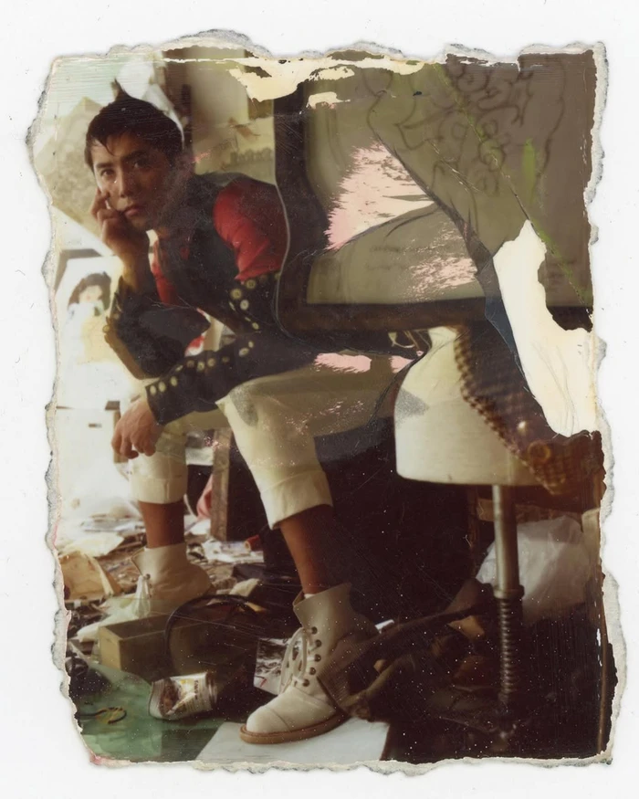 Man seated on a stool wearing red shirt and white trousers with distressed photo borders by Mark Lebon
