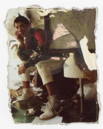 Man seated on a stool wearing red shirt and white trousers with distressed photo borders by Mark Lebon