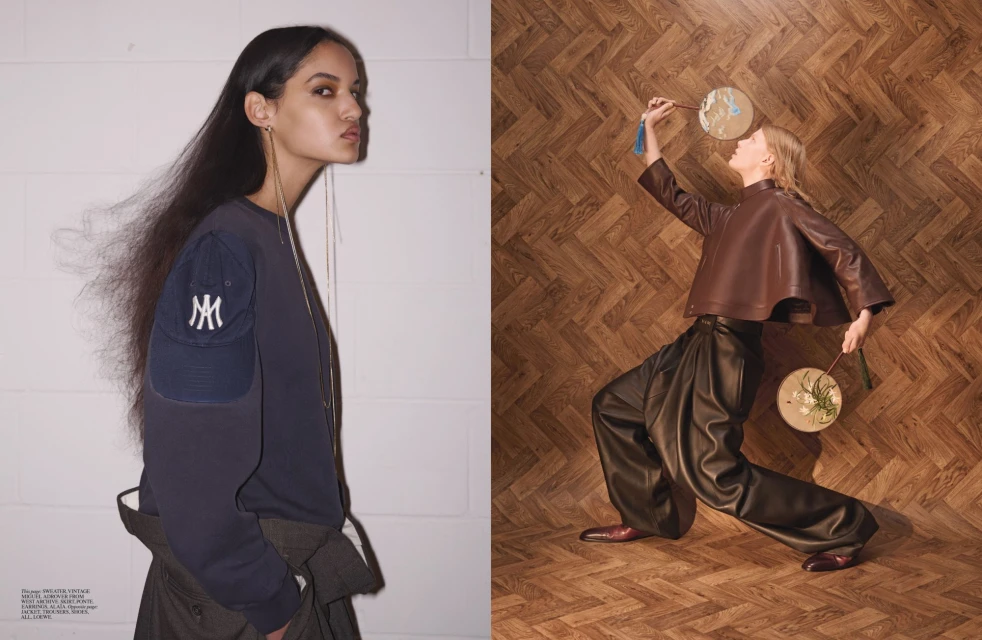 Two models pose against a neutral backdrop, one in a navy sweater and the other in a brown leather top and black pants.