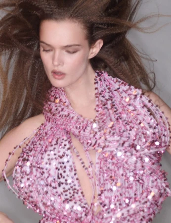 Close-up of a female model with crimped long brown hair wearing a sparkling pink beaded halter top, posing in a photo studio.