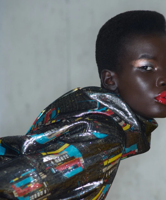 Close-up studio shot of a dark-skinned female model wearing a patterned shiny top with red lipstick and metallic eyeshadow.