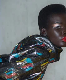 Close-up portrait of a black woman wearing a metallic patterned hooded top with bright red lips, photographed by Johnny Dufort.