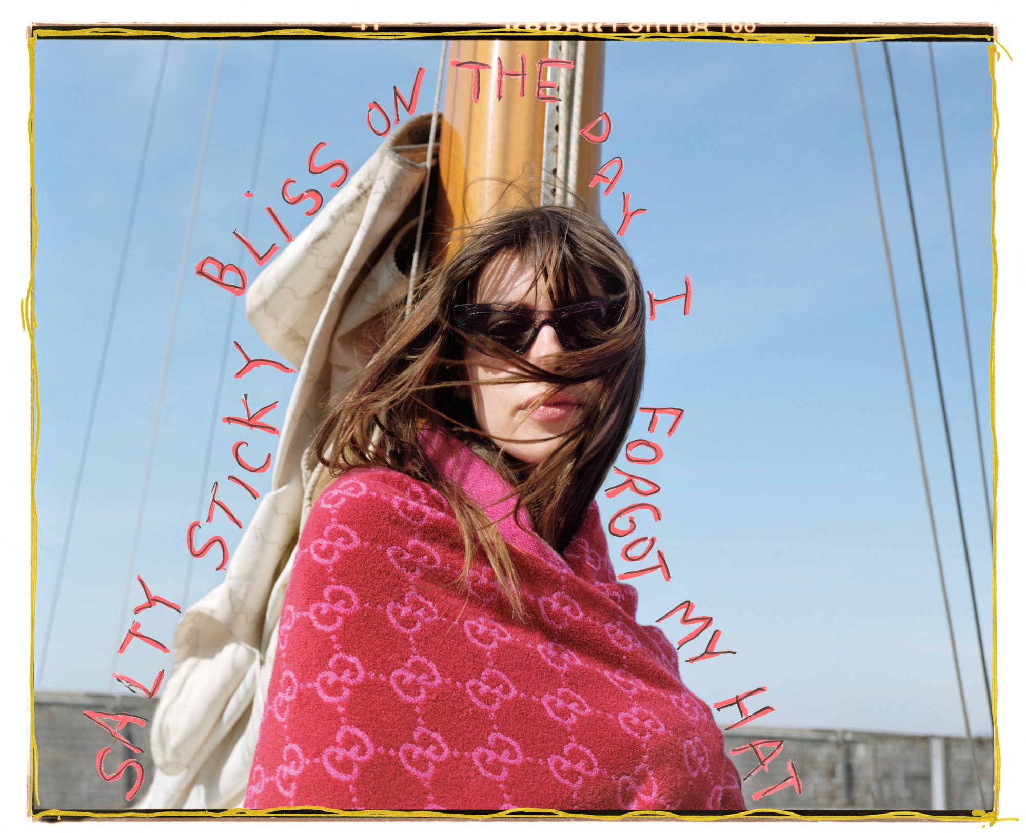Woman with a red patterned shawl and sunglasses on a sailboat. She is facing forward with blue sky and mast behind her.