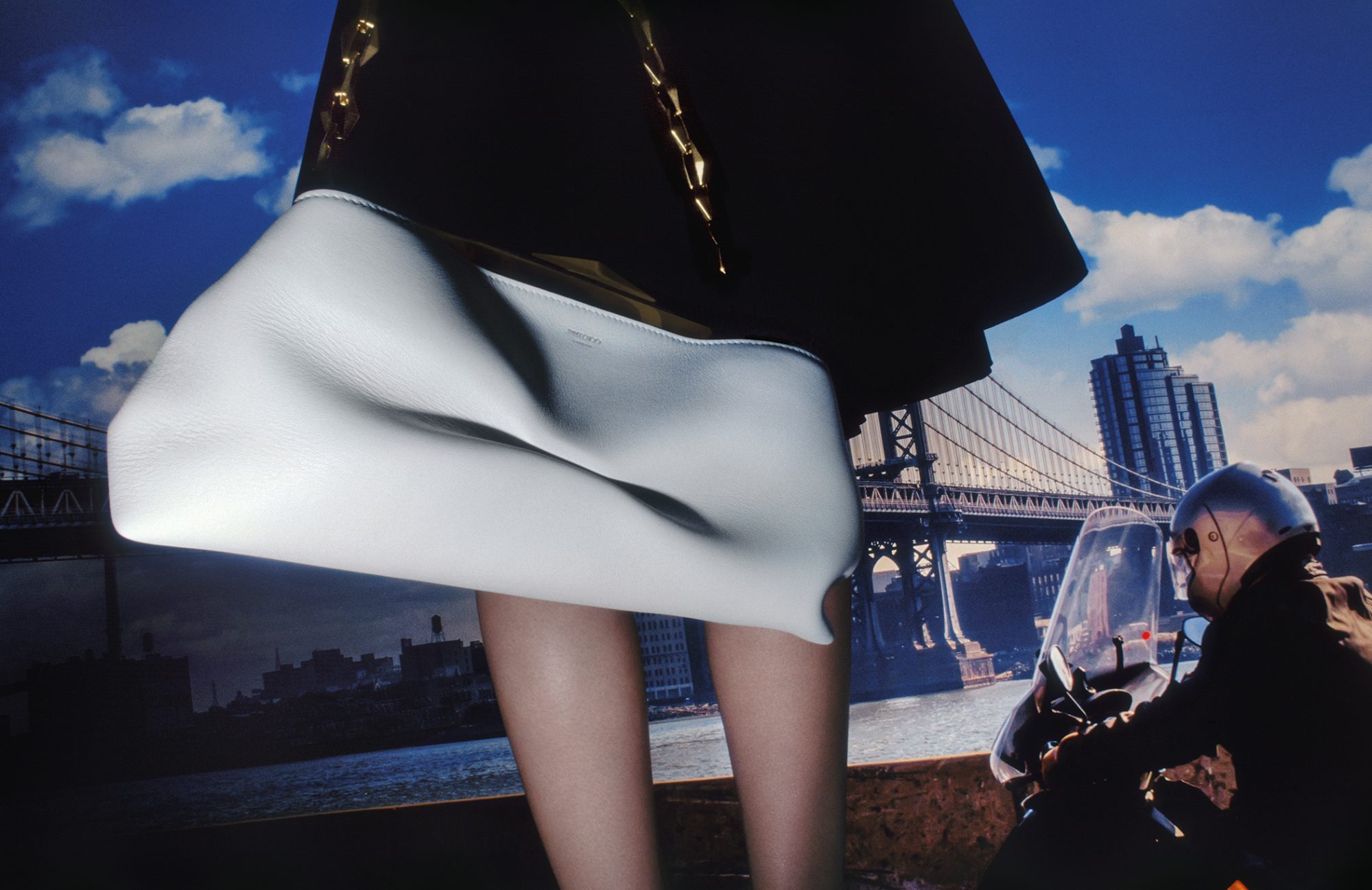 White leather handbag in a fashion setting with a motorcyclist and the Manhattan Bridge in the background, creating an urban backdrop.