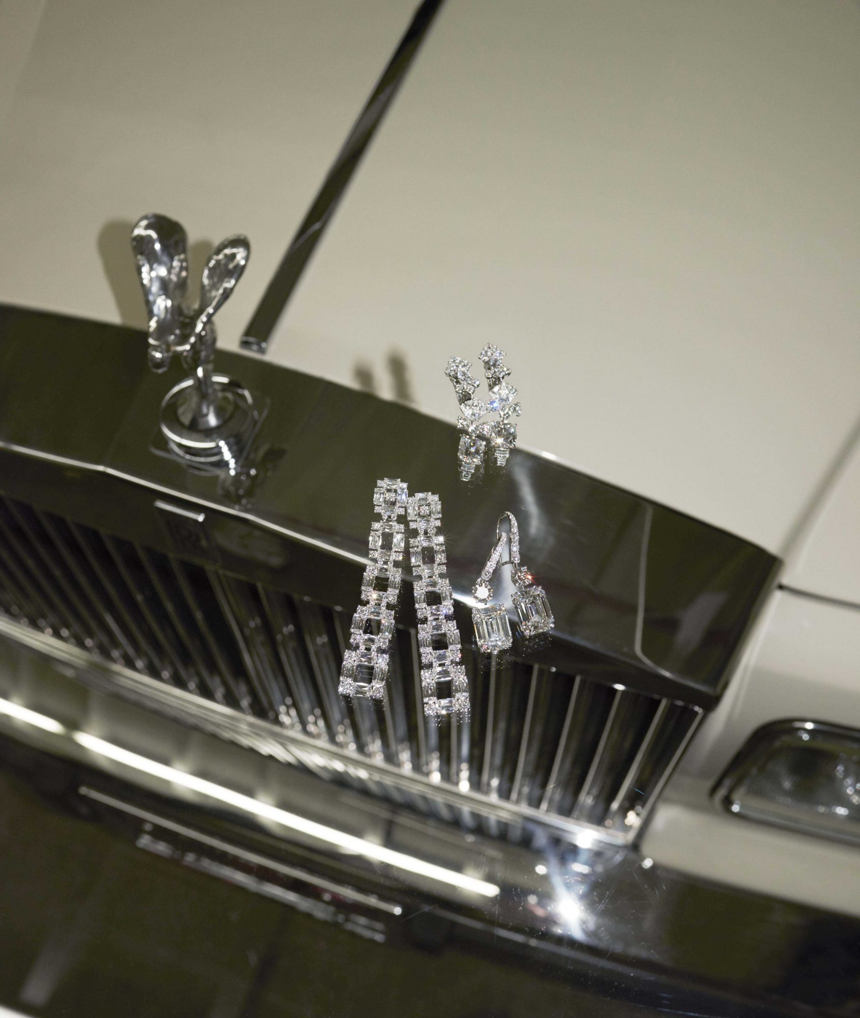 Sparkling diamond jewelry, including earrings and a ring, displayed on the hood of a classic white Rolls Royce car.