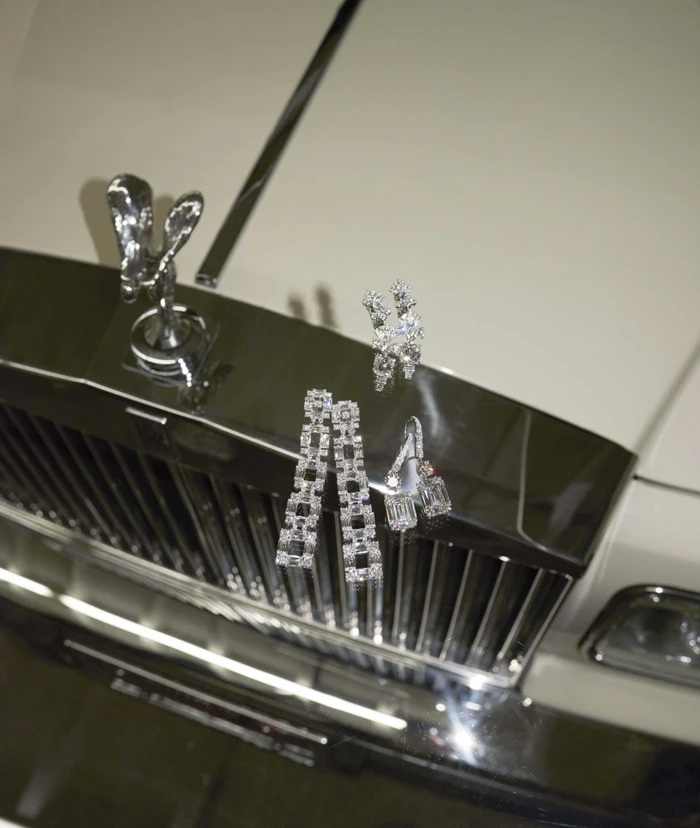 Sparkling diamond jewellery pieces arranged carefully on the chrome grille and hood of a luxury car.
