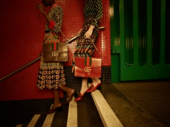 Two women holding leather shoulder bags with interlocking logos while walking down tiled stairs by photographer Jack Webb.