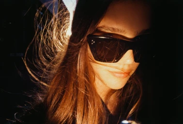 Close-up portrait of a woman wearing dark sunglasses with light catching her hair by photographer Jack Webb