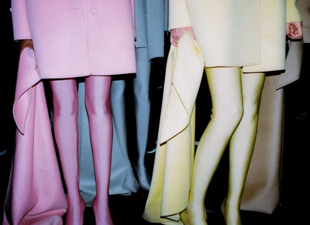 Fashion models in pastel-colored outfits showcase hosiery. Lower torsos and legs are visible, with a fashion show or studio background.
