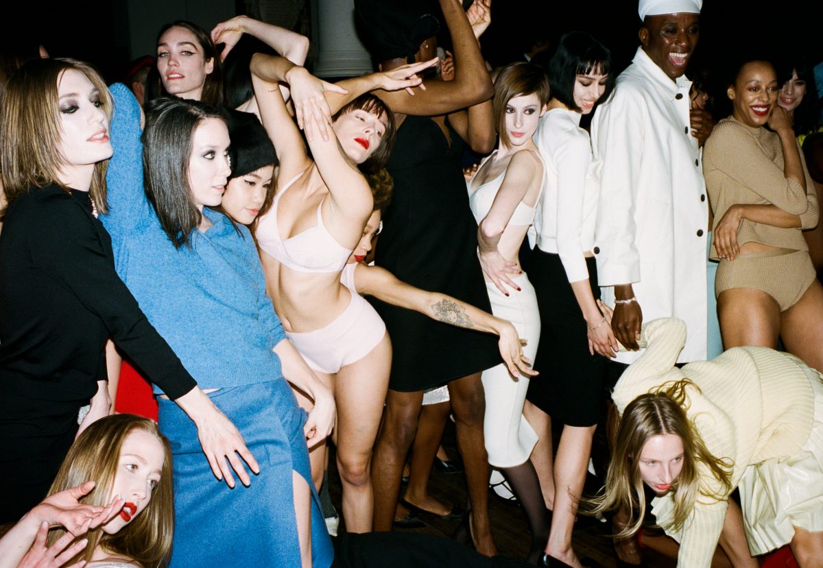 Diverse group of models pose indoors wearing modern clothing, standing close together, with bright, even lighting and a medium shot.