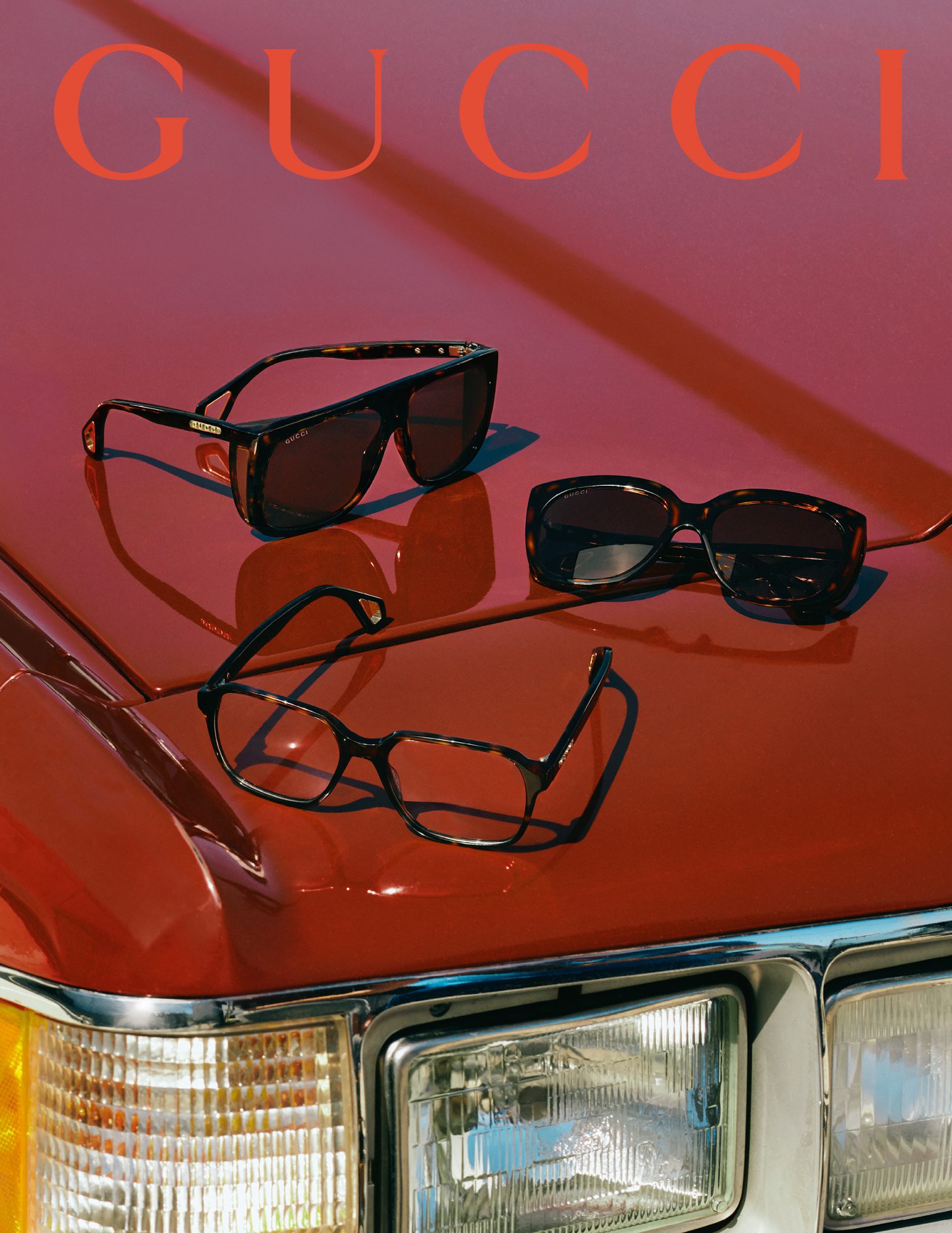 Three pairs of sunglasses are displayed on the hood of a red car, with the brand name GUCCI visible in orange text above.