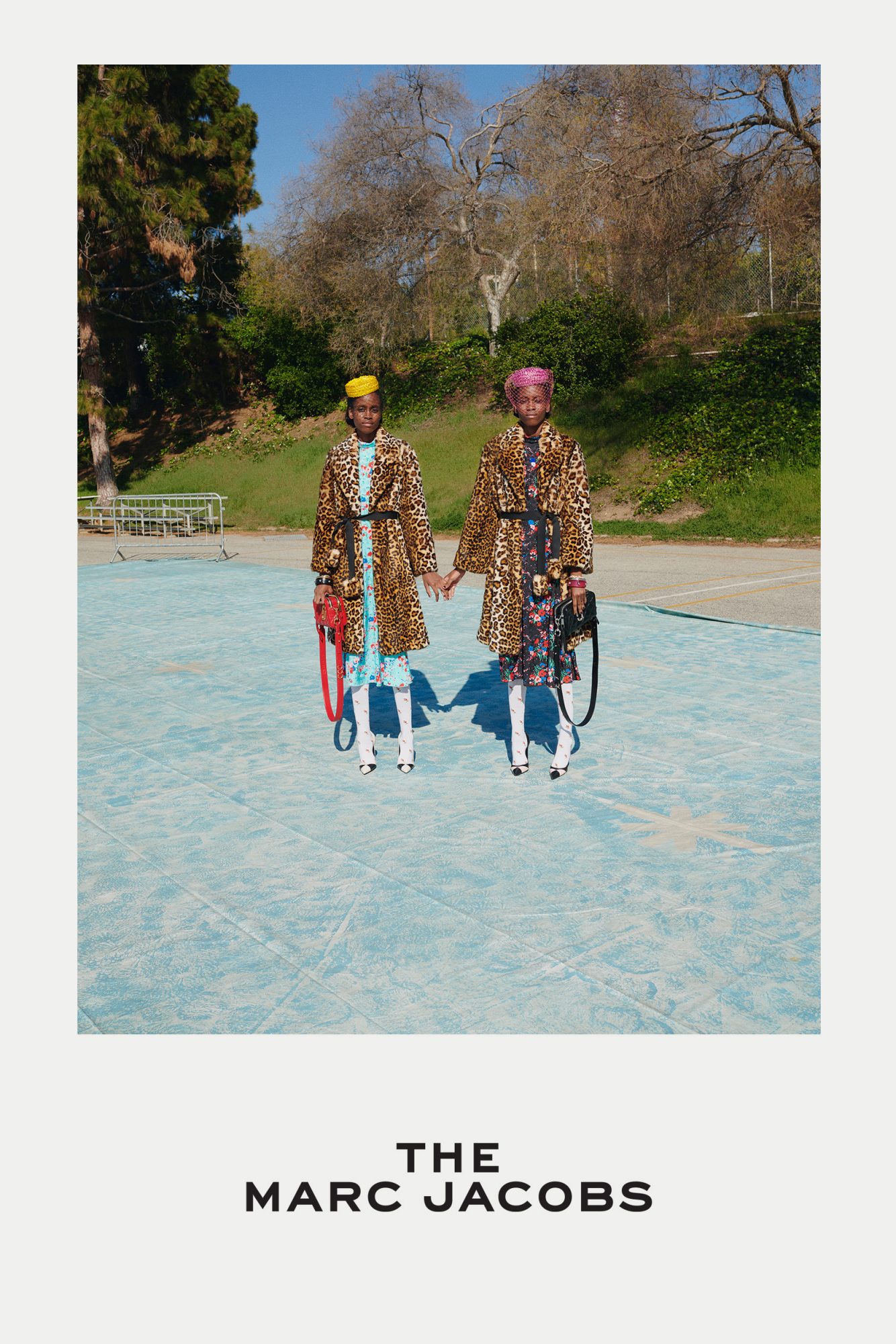 Two fashionably dressed Black women in leopard print coats hold hands on a blue court, accessorized with hats, bags, and white boots.
