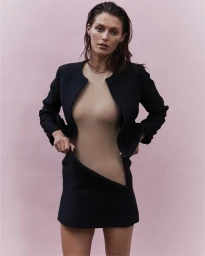 Model in a black jacket and matching miniskirt with wet hair standing against a pale pink background.