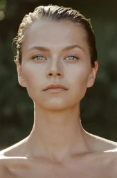 Close-up portrait of a woman with slicked-back wet hair and striking blue eyes against a soft natural background.