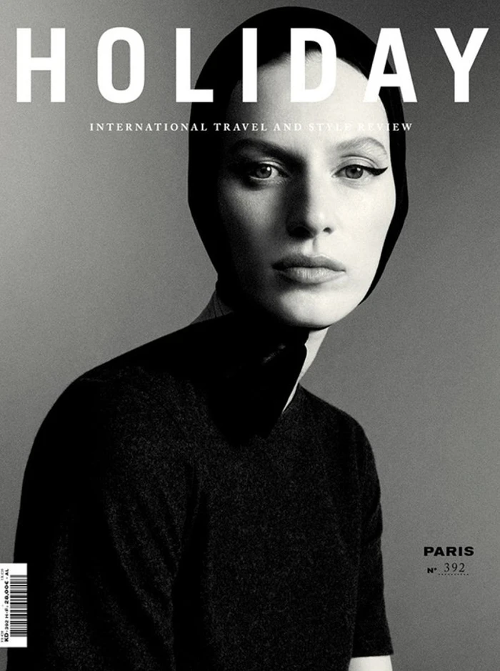 Monochrome magazine cover portrait of a woman wearing a black head covering and dark top against a grey background.