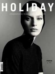 Monochrome magazine cover portrait of a woman wearing a black head covering and dark top against a grey background.