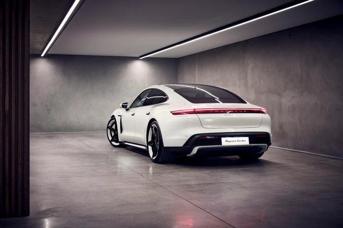 Rear view of a white Porsche Taycan Turbo parked in a garage with bright overhead lighting and a smooth concrete floor.