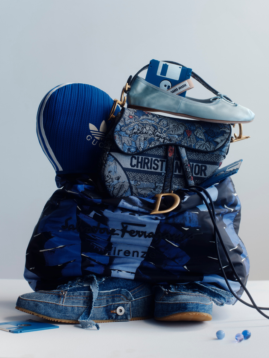 Stack of designer fashion items including a Dior handbag, Adidas hat, Ferragamo jacket, denim sneakers, and floppy disk.