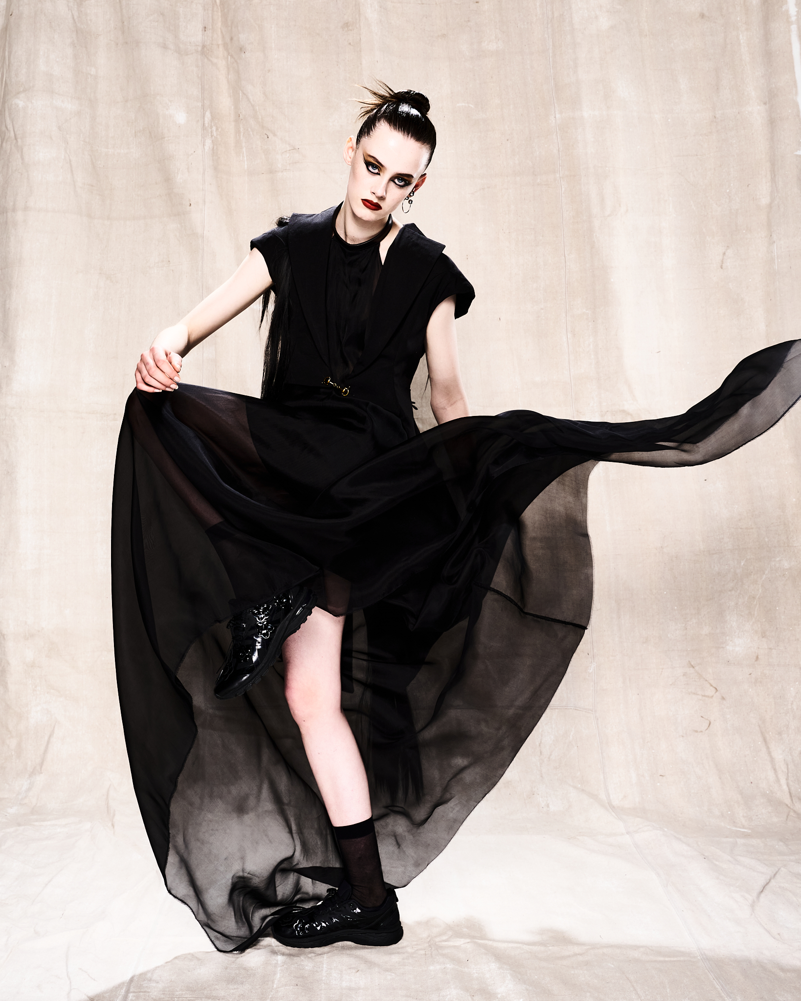 Woman posing dramatically in a flowing black gown in a studio setting, showcasing high fashion and dark, elegant aesthetics.