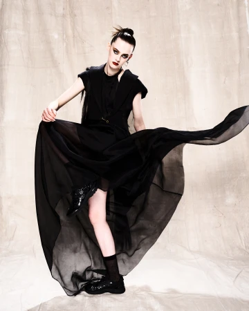 Woman posing dramatically in a flowing black gown in a studio setting, showcasing high fashion and dark, elegant aesthetics.