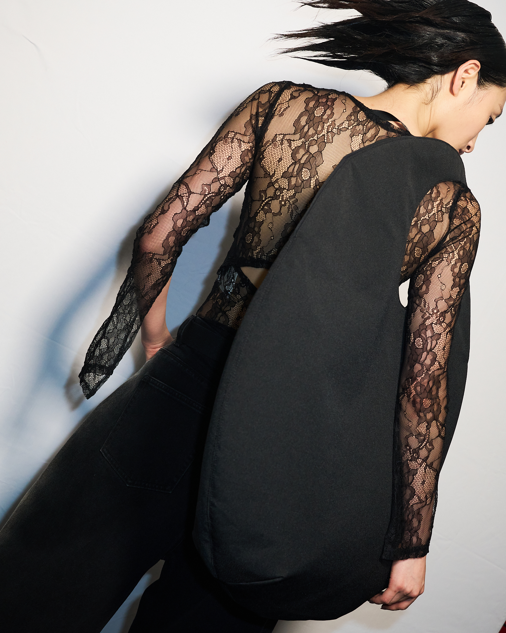 Fashion shot of an adult woman posing indoors wearing a black lace top, black jeans and carrying a black soft leather bag.