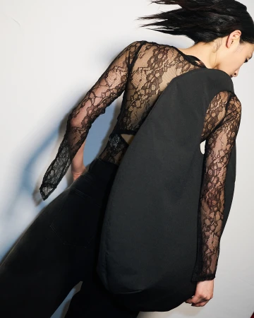 Fashion shot of an adult woman posing indoors wearing a black lace top, black jeans and carrying a black soft leather bag.