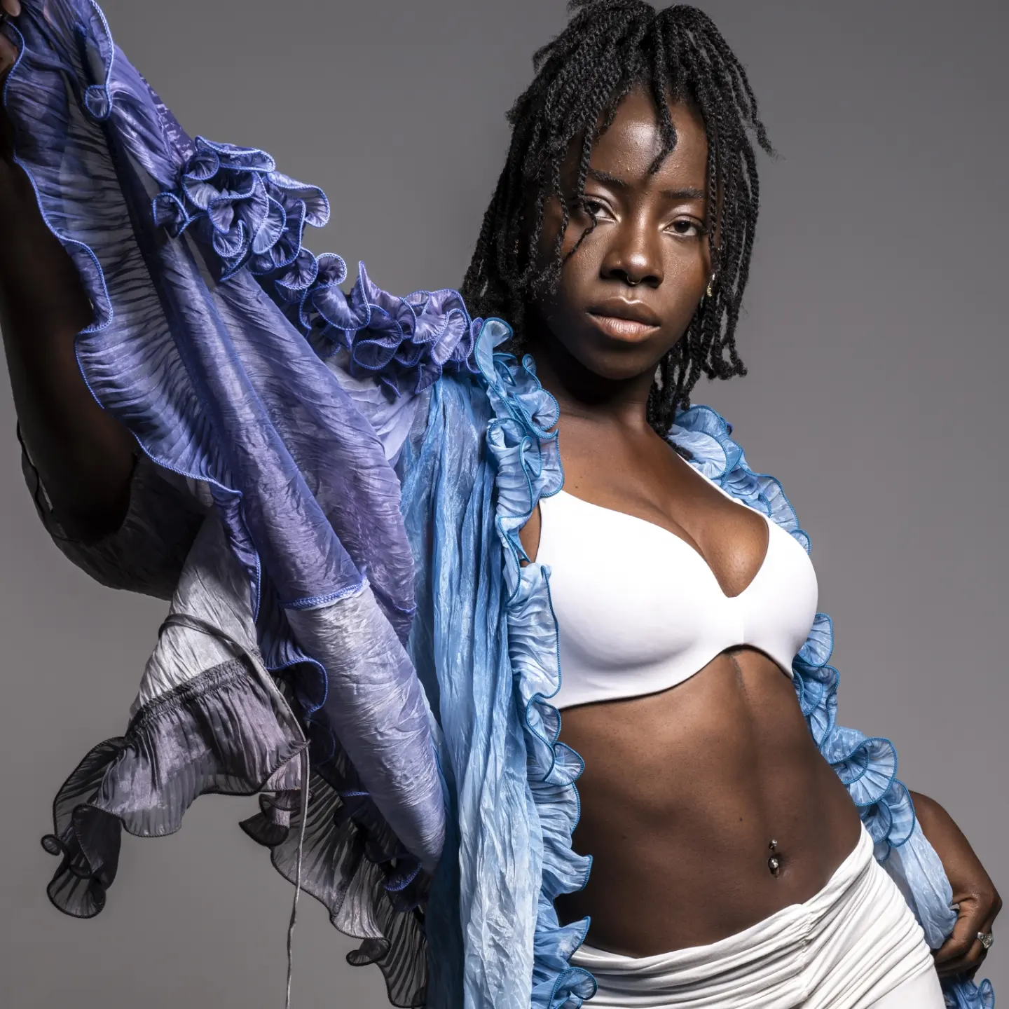 Elegant portrait of a woman with dark skin, wearing a white top and a translucent, flowing blue shawl in a studio setting.