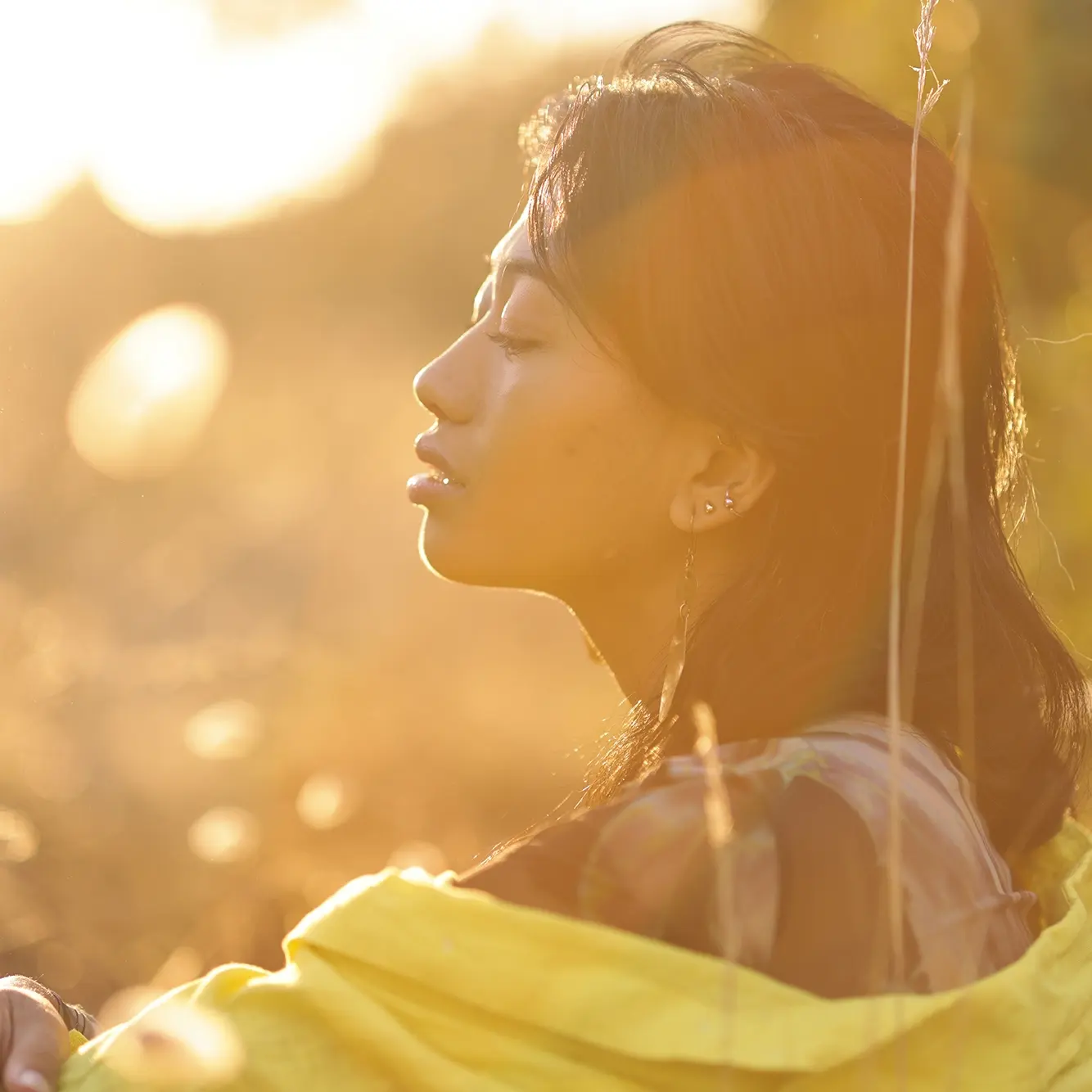 Profile portrait of a young woman outdoors at sunset with warm backlight and glowing golden hour light.