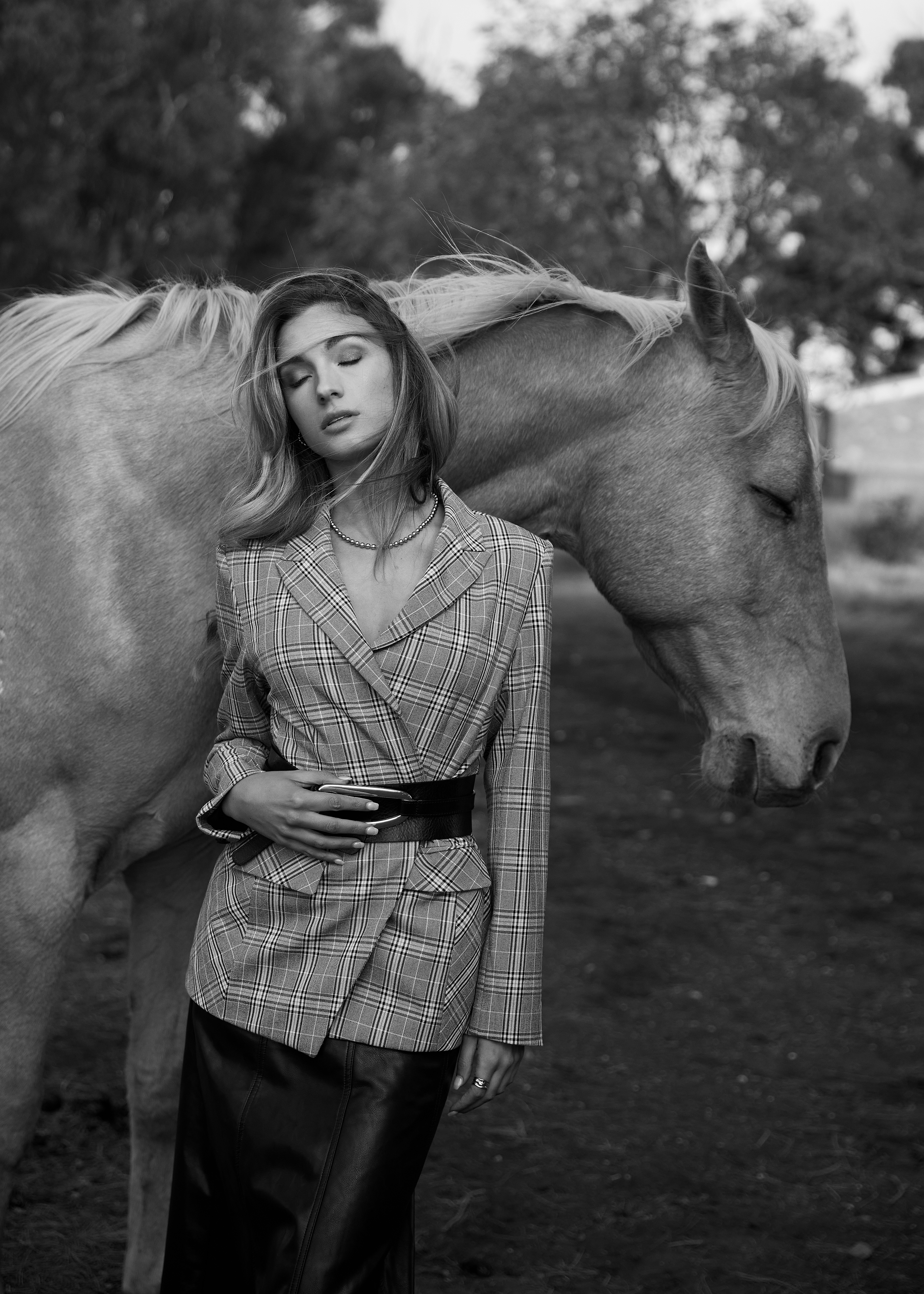 Black and white portrait of a woman in a plaid blazer standing next to a horse outdoors