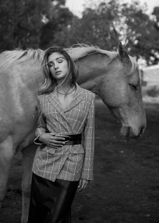 Black and white portrait of a woman in a plaid blazer standing next to a horse outdoors