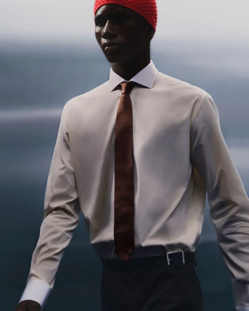 A person wearing a white collared shirt, brown tie, and red knit cap against a blurry background in a fashion style image.