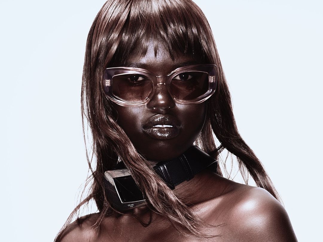 Portrait of a woman wearing translucent sunglasses and a black leather choker against a white background