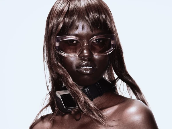 Portrait of a woman wearing translucent sunglasses and a black leather choker against a white background