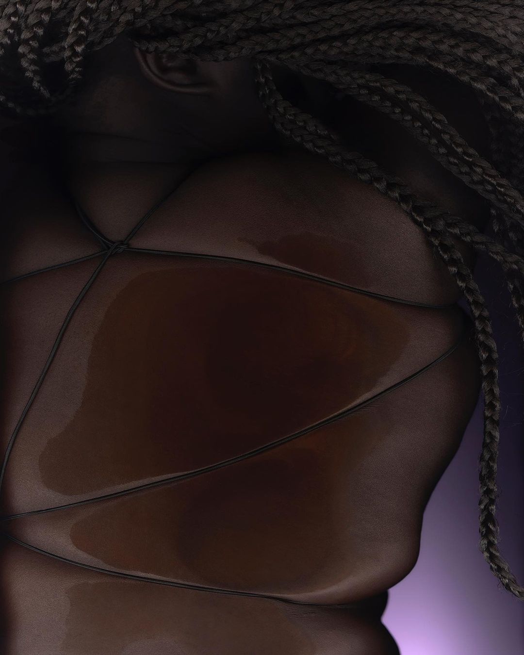 Close-up of a person's upper torso wearing a black body stocking and braided hair, with a purple backdrop creating a studio portrait.
