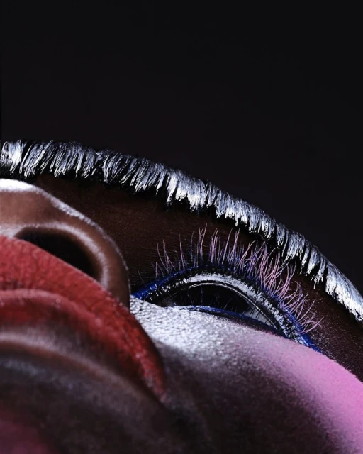 Close-up studio shot of a Black female with silver-painted hair, artistic pink, and blue makeup, and dramatic eyelashes.
