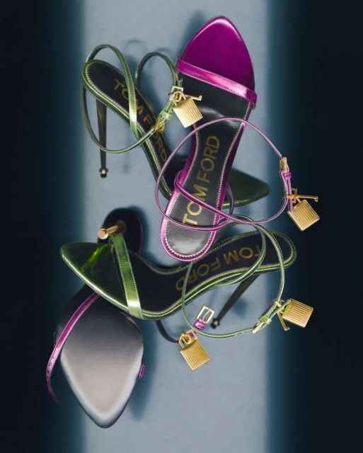 Elevated view of Tom Ford high heel sandals in pink and green metallic leather with signature gold padlock detail on a gradient background.