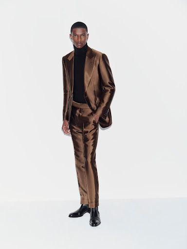 Full-length shot of a Black male model in a bronze suit with a black turtleneck against a white background in a fashion style image.