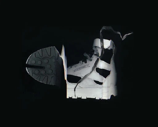 High-top Reebok sneaker cut in half, showing sole and shoe profile, illuminated against a black background.